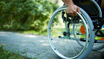 Close-up of male hand on wheel of wheelchair during walk in park